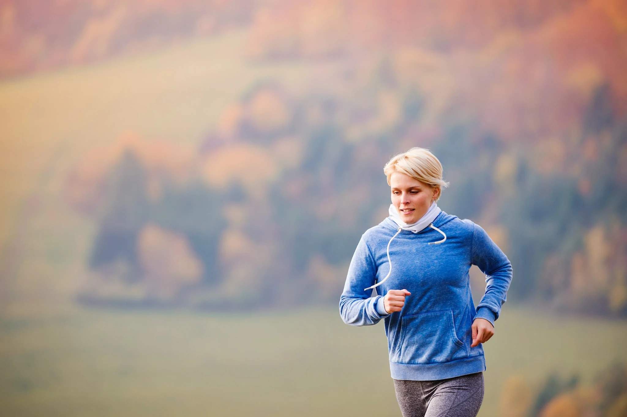 A woman jogging outdoors in a blue hoodie