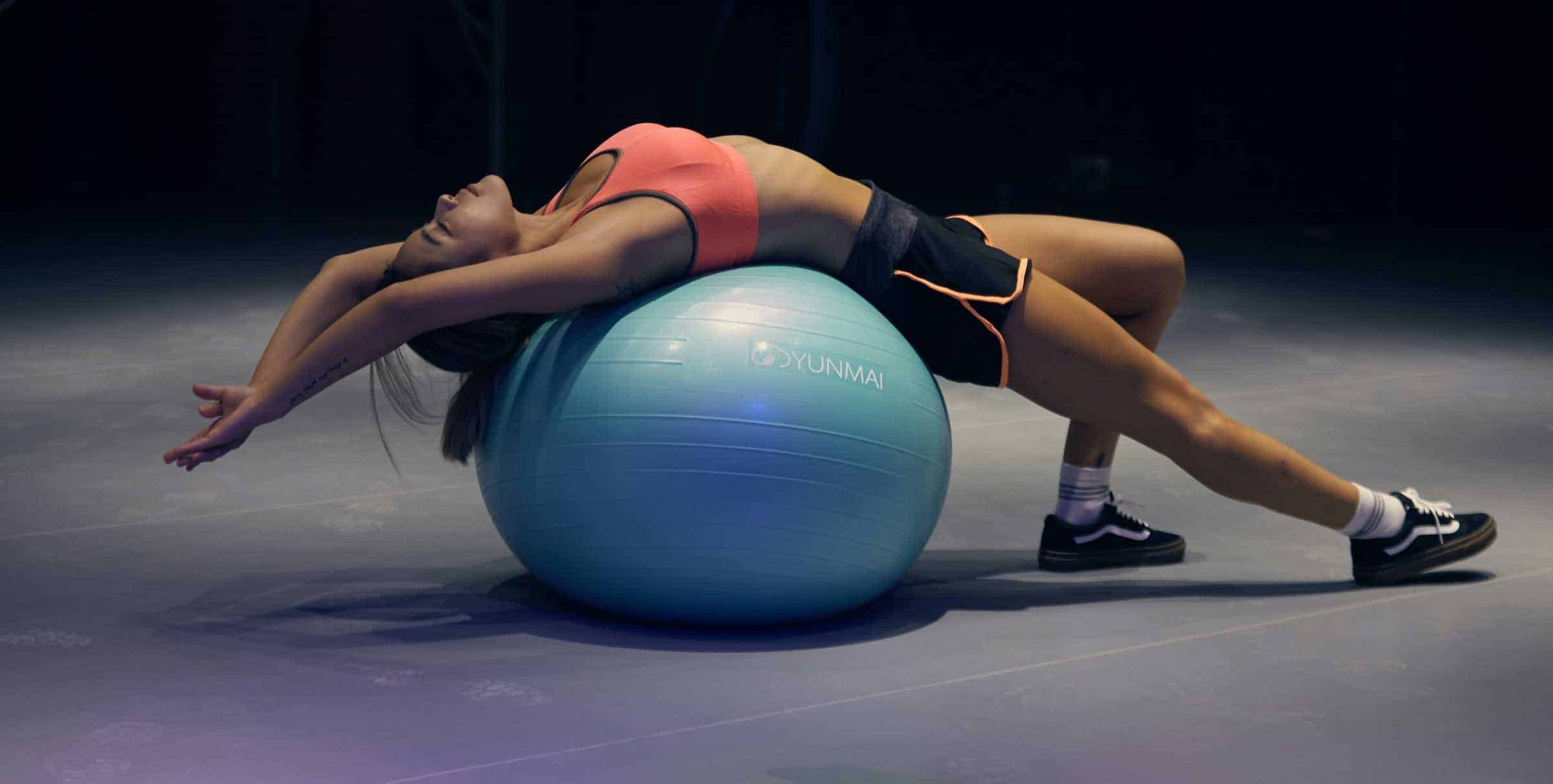 A woman stretching her back over a stability ball