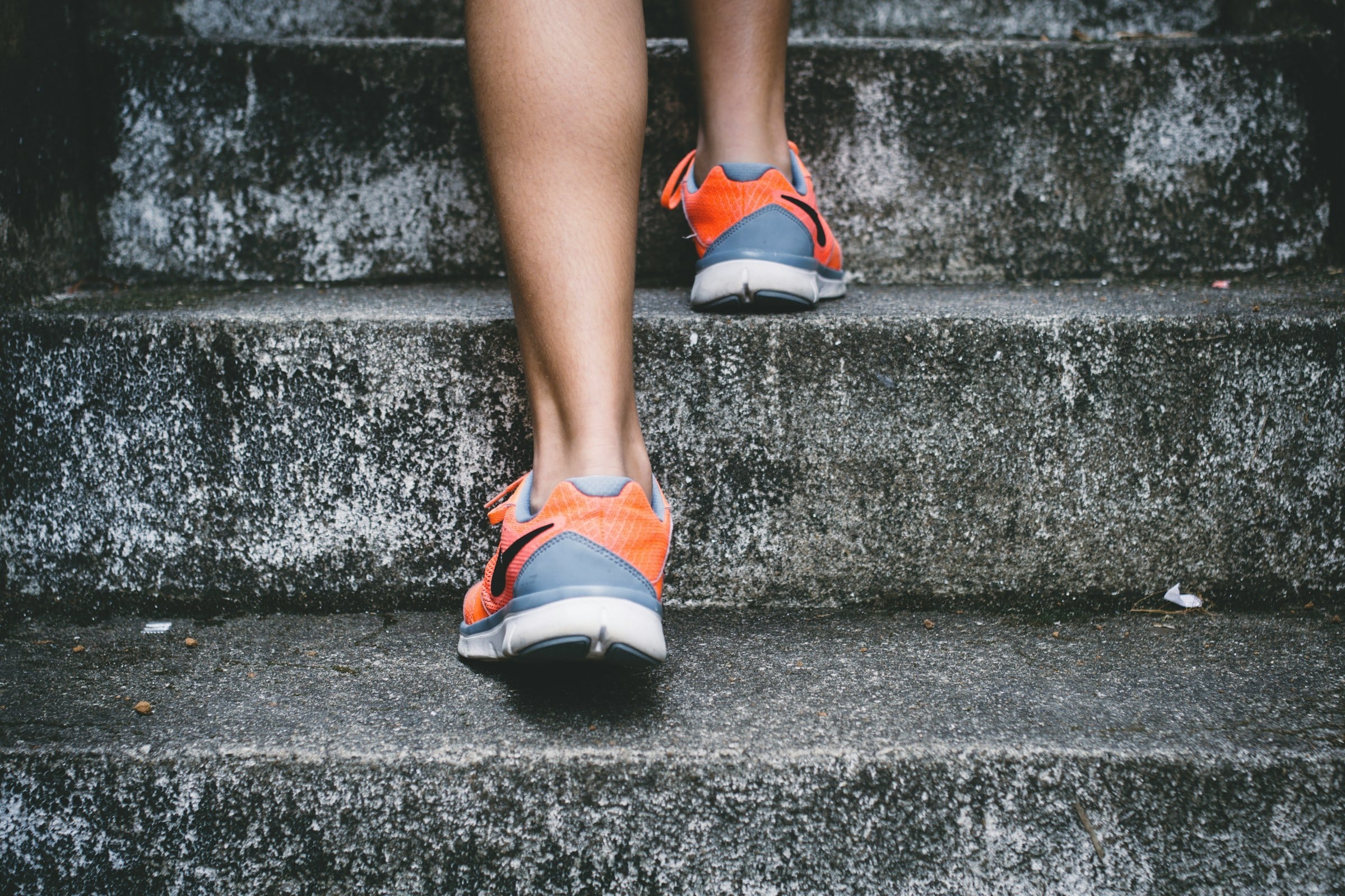 Close-up of a person in orange running shoes climbing outdoor stone steps