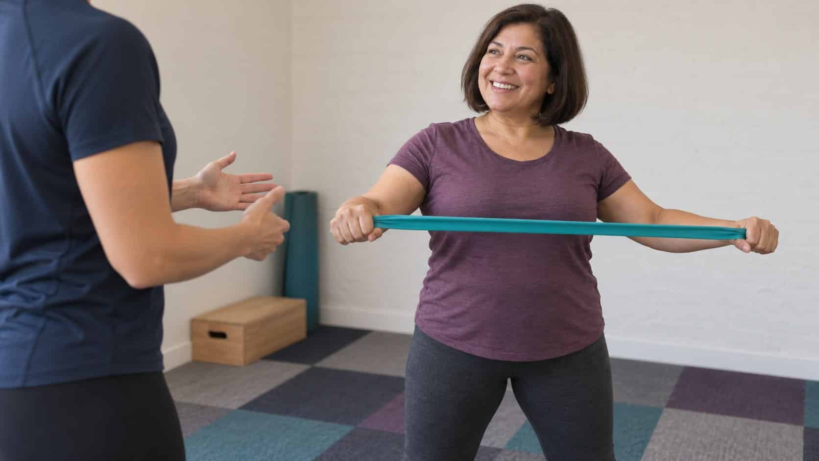 A woman using a resistance band while a trainer guides her